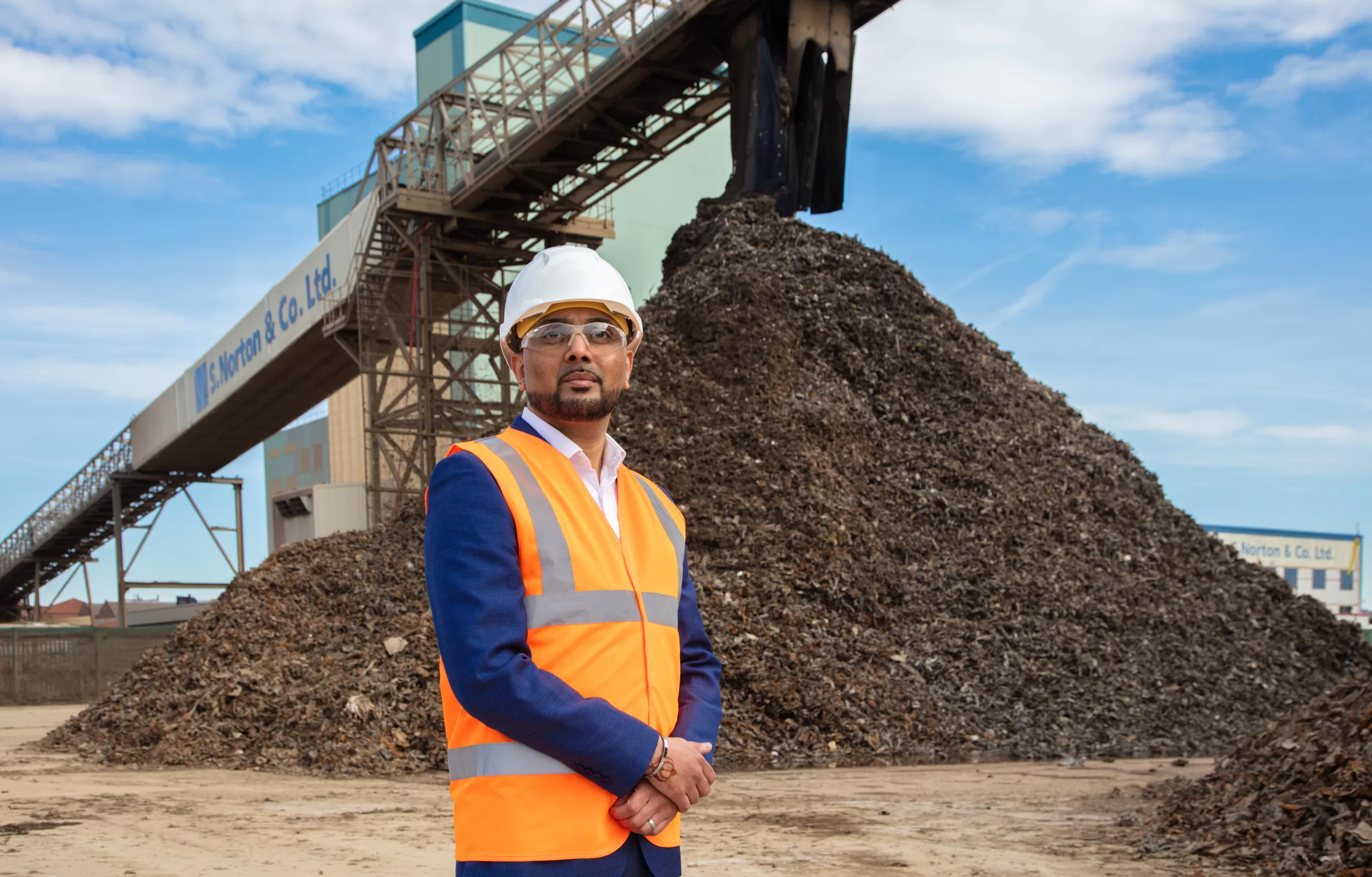 Managing Director of S Norton, Tony Hayer is pictured in front of pile of scrap metal in a high-vis vest, hard hat and goggles